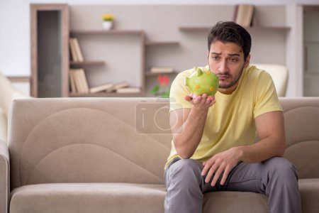 Photo for Young man holding piggybank at home - Royalty Free Image