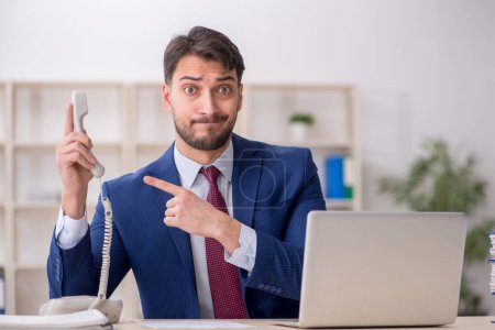 Téléchargez les photos : Jeune employé parlant par téléphone sur le lieu de travail - en image libre de droit