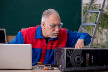 Photo for Old male repairman repairing computers in the classroom - Royalty Free Image