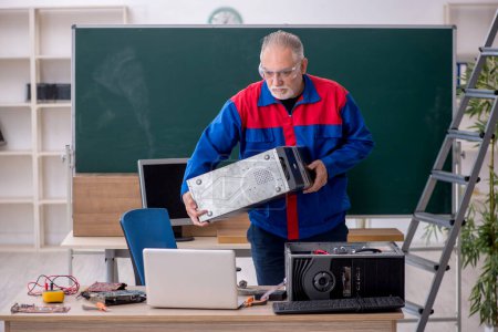 Photo for Old male repairman repairing computers in the classroom - Royalty Free Image
