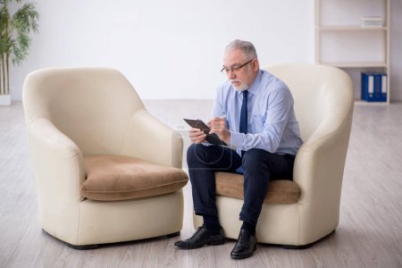Téléchargez les photos : Vieux psychologue masculin assis sur un fauteuil - en image libre de droit