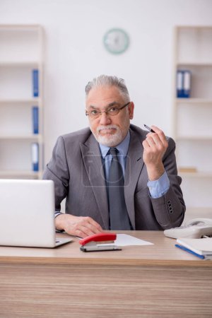 Téléchargez les photos : Old employee sitting at workplace - en image libre de droit