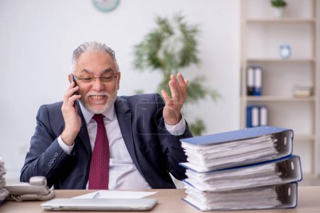 Téléchargez les photos : Old employee speaking by phone at workplace - en image libre de droit