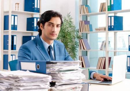 Téléchargez les photos : Le jeune bel employé masculin avec trop de travail au bureau - en image libre de droit
