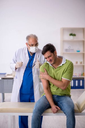 Foto de Paciente joven que visita al viejo médico en concepto de vacunación - Imagen libre de derechos