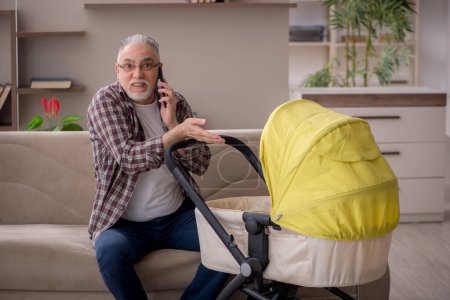 Téléchargez les photos : Old man looking after baby at home - en image libre de droit