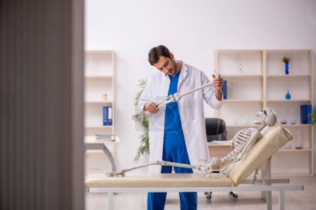 Téléchargez les photos : Jeune homme médecin avec squelette à l'hôpital - en image libre de droit