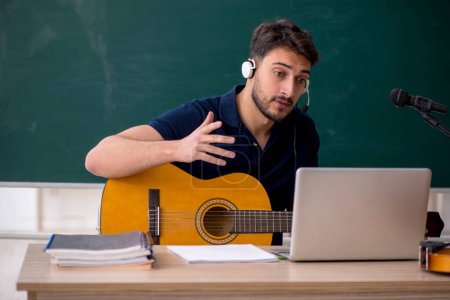 Téléchargez les photos : Jeune professeur de musique assis dans la salle de classe - en image libre de droit