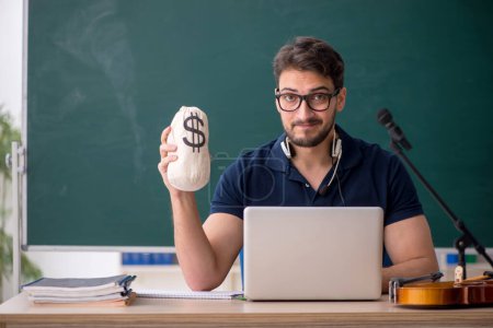 Photo for Young music teacher holding moneybag in the classroom - Royalty Free Image