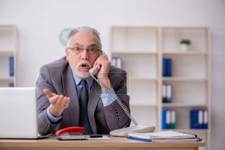 Foto de Old employee speaking by phone at workplace - Imagen libre de derechos