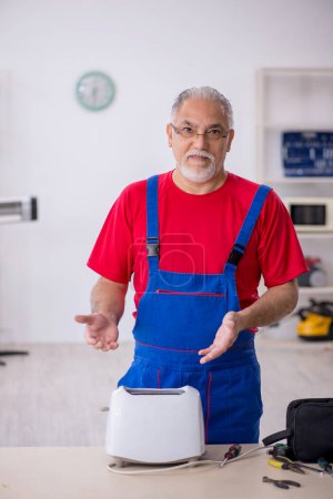 Photo for Old male repairman repairing toaster at workshop - Royalty Free Image