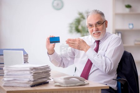 Photo for Old employee holding credit card at workplace - Royalty Free Image