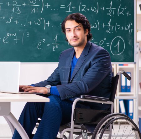 Téléchargez les photos : The young handsome man in wheelchair in front of chalkboard - en image libre de droit