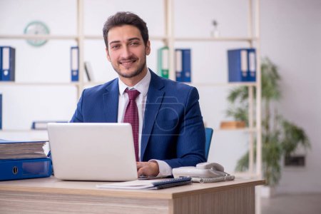 Photo for Young businessman employee and too much work at workplace - Royalty Free Image