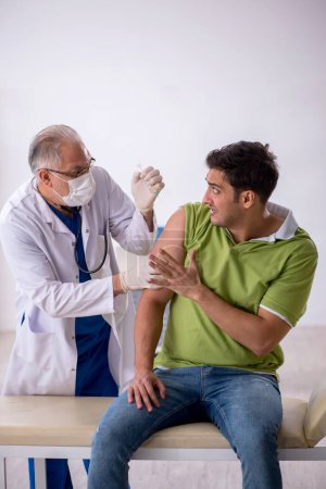 Téléchargez les photos : Jeune patient visitant un vieux médecin dans le concept de vaccination - en image libre de droit