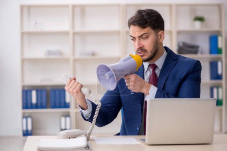 Photo for Young employee holding megaphone at workplace - Royalty Free Image