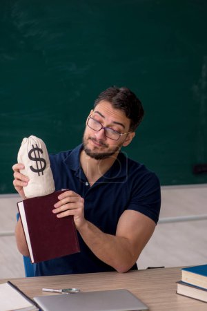 Foto de Joven profesor sosteniendo bolsa de dinero en el aula - Imagen libre de derechos