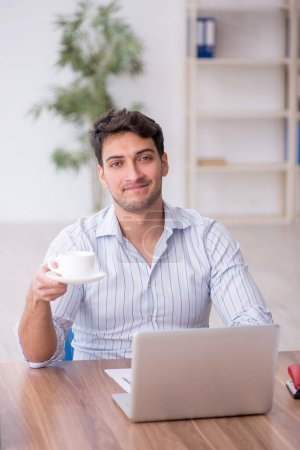 Téléchargez les photos : Jeune employé buvant du café pendant le petit déjeuner - en image libre de droit