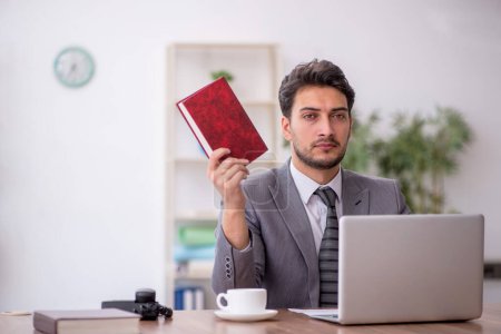 Téléchargez les photos : Jeune employé livre de lecture dans le bureau - en image libre de droit