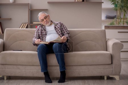 Foto de Old man reading book at home during pandemic - Imagen libre de derechos