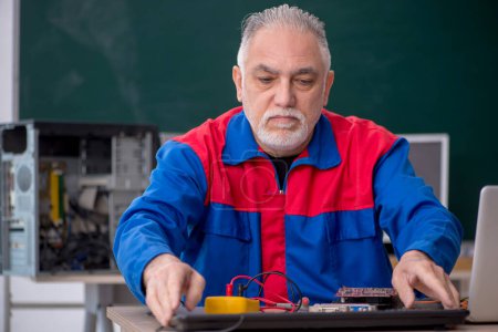 Foto de Hombre viejo reparador reparando computadoras en el aula - Imagen libre de derechos