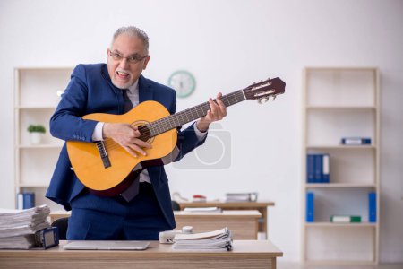 Foto de Old employee playing guitar in the office - Imagen libre de derechos