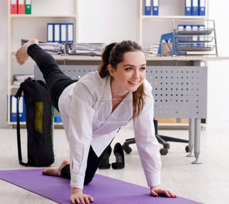 Foto de The female employee doing sport exercises in the office - Imagen libre de derechos
