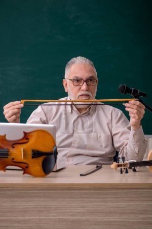 Photo for Old teacher playing violin in the classroom - Royalty Free Image
