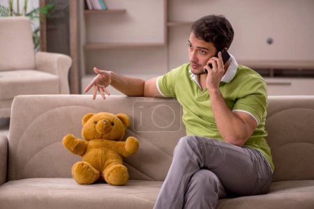 Téléchargez les photos : Jeune étudiant mâle avec ours jouet à la maison - en image libre de droit