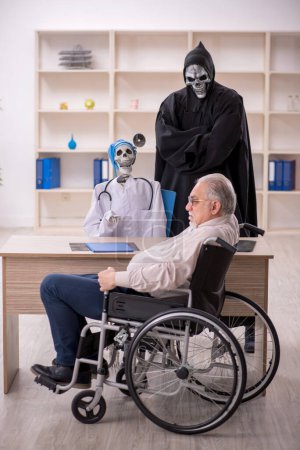 Foto de Viejo paciente masculino en silla de ruedas visitando a dos doctores diabólicos - Imagen libre de derechos