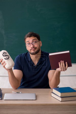 Foto de Joven profesor sosteniendo bolsa de dinero en el aula - Imagen libre de derechos