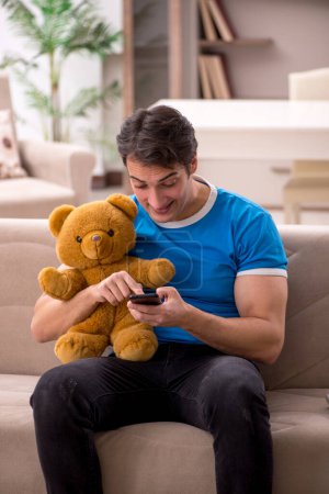 Téléchargez les photos : Jeune homme assis avec jouet ours à la maison - en image libre de droit