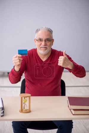 Téléchargez les photos : Old teacher holding credit card in the office - en image libre de droit