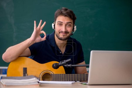 Téléchargez les photos : Jeune professeur de musique assis dans la salle de classe - en image libre de droit
