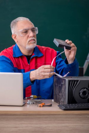 Téléchargez les photos : Vieux réparateur masculin réparant des ordinateurs dans la salle de classe - en image libre de droit