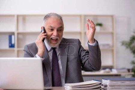 Photo for Old employee speaking by phone at workplace - Royalty Free Image