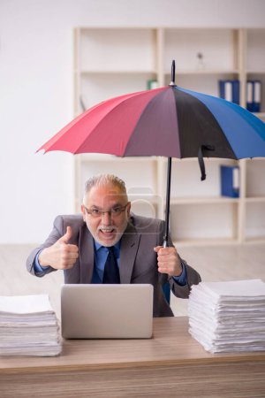 Foto de Old employee holding an umbrella at workplace - Imagen libre de derechos