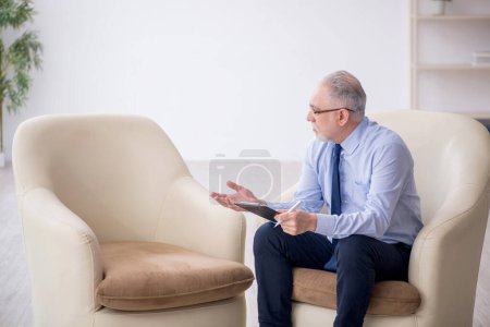 Téléchargez les photos : Vieux psychologue masculin assis sur un fauteuil - en image libre de droit