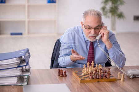Foto de Viejo empleado jugando ajedrez en la oficina - Imagen libre de derechos