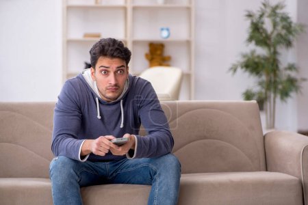 Téléchargez les photos : Jeune étudiant mâle regarder la télévision à la maison - en image libre de droit
