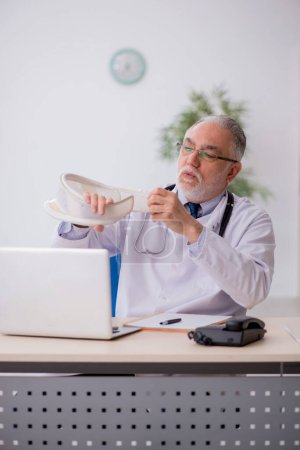 Foto de Un viejo doctor sosteniendo un corsé en la clínica - Imagen libre de derechos