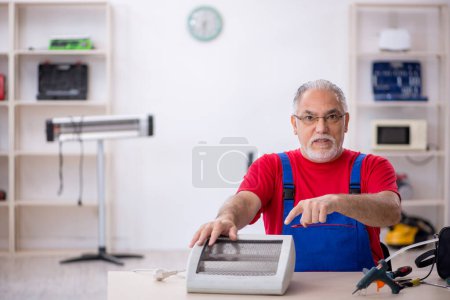 Photo for Old male repairman repairing heater at workshop - Royalty Free Image