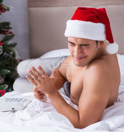 Foto de El hombre sexy en la cama con sombrero de santa en el concepto de Navidad - Imagen libre de derechos