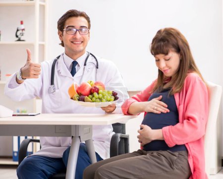 Foto de La mujer embarazada que visita al médico discutiendo dieta saludable - Imagen libre de derechos