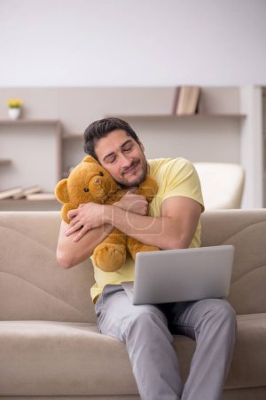 Foto de Joven estudiante masculino abrazando juguete oso en casa - Imagen libre de derechos