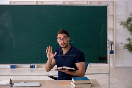 Téléchargez les photos : Jeune enseignant assis dans la salle de classe - en image libre de droit