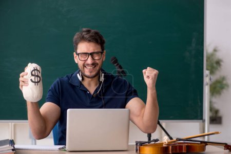 Téléchargez les photos : Jeune professeur de musique tenant sac d'argent dans la salle de classe - en image libre de droit