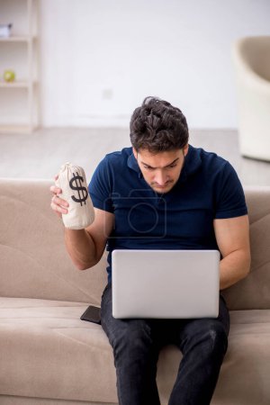 Photo for Young male freelancer holding moneybag at home - Royalty Free Image