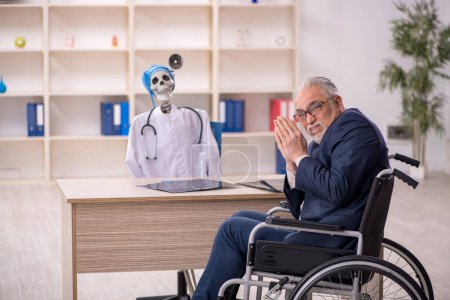 Photo for Old male patient in wheel-chair visiting devil doctor - Royalty Free Image