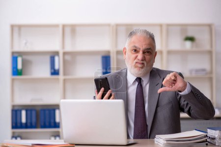Téléchargez les photos : Old employee speaking by phone at workplace - en image libre de droit